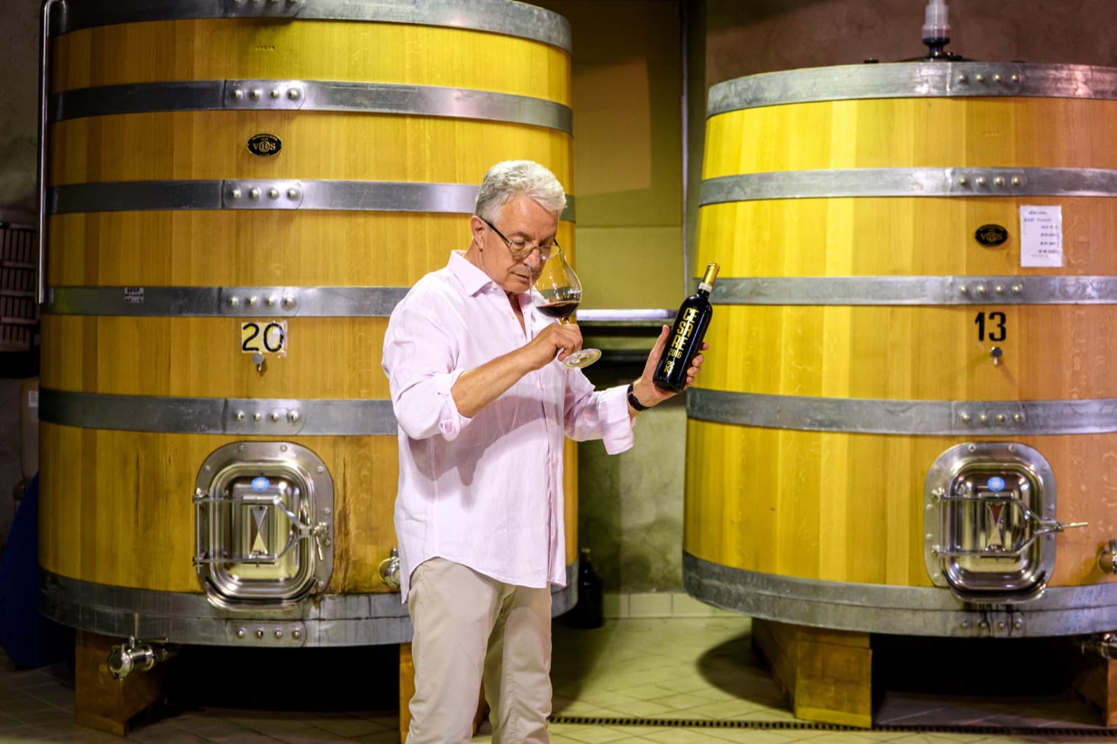 Emanuele Anzivino esamina il vino al calice accanto ai grandi tini di rovere