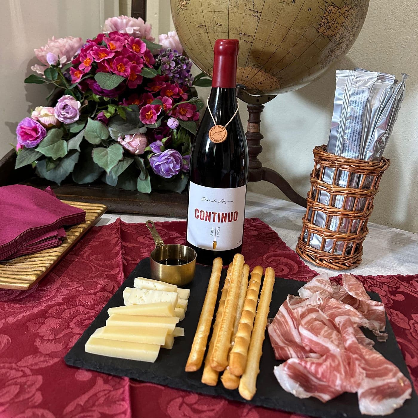 Il tagliere della degustazione: formaggi e salumi locali con grissini, accanto a una bottiglia di Continuo